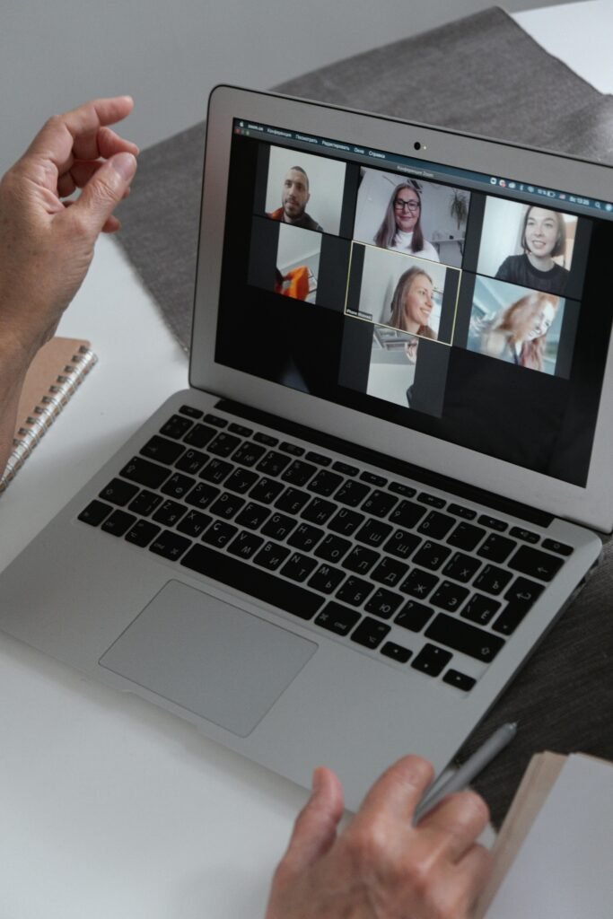 Home Hands at a laptop showing a group video call in a home office setting.